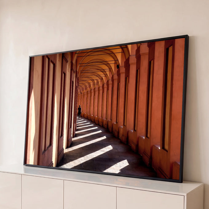 Corredor de arcos em Bolonha, tons terracota, sombras diagonais e pessoa caminhando, quadro decorativo