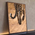Close das patas e cauda malhada de leopardo caminhando sobre areia clara em tons bege, quadro decorativo
