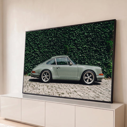 Porsche 911 clássico verde sálvia de perfil diante de muro de hera sobre piso de pedras, quadro decorativo