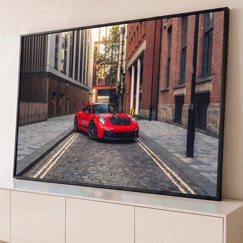 Porsche 911 GT3 RS vermelho estacionado em beco de paralelepípedos entre prédios de tijolo, quadro decorativo