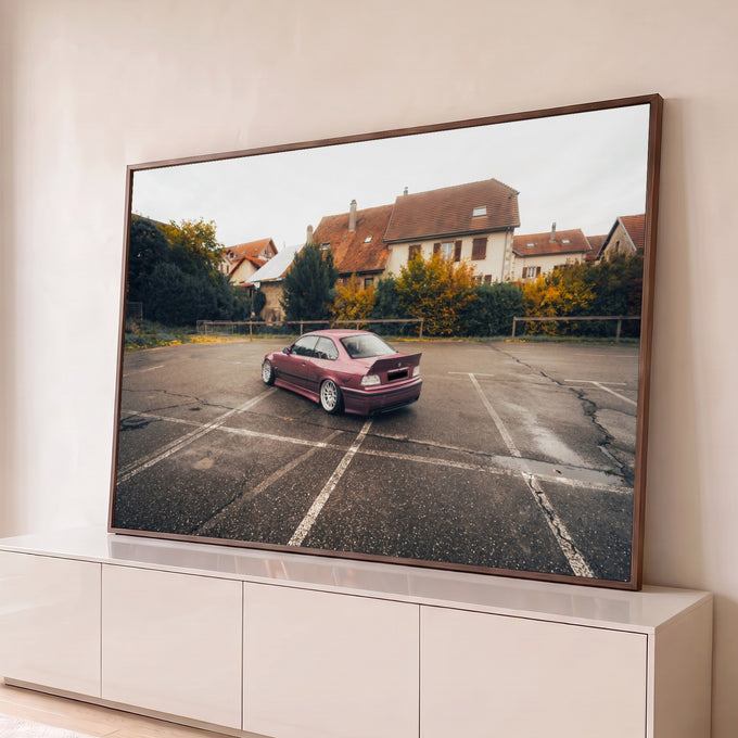 Carro esportivo rebaixado bordô em estacionamento molhado com casas europeias e árvores de outono, quadro decorativo