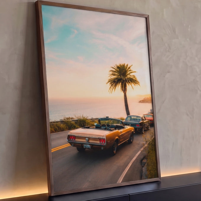 Carro conversível vintage dourado em estrada litorânea ao pôr do sol com palmeira e mar, quadro decorativo