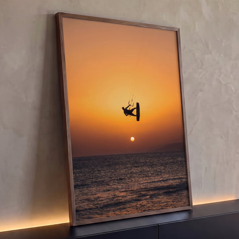 Silhueta de kitesurfista saltando sobre o mar com sol no horizonte e céu laranja, quadro decorativo