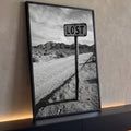 Placa Lost em poste de madeira numa estrada de terra no deserto com montanhas, foto P&B, quadro decorativo