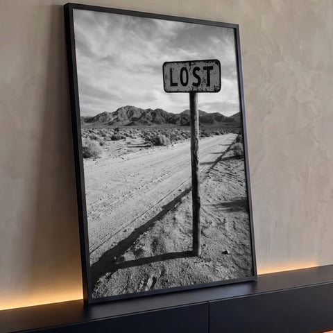 Placa Lost em poste de madeira numa estrada de terra no deserto com montanhas, foto P&B, quadro decorativo