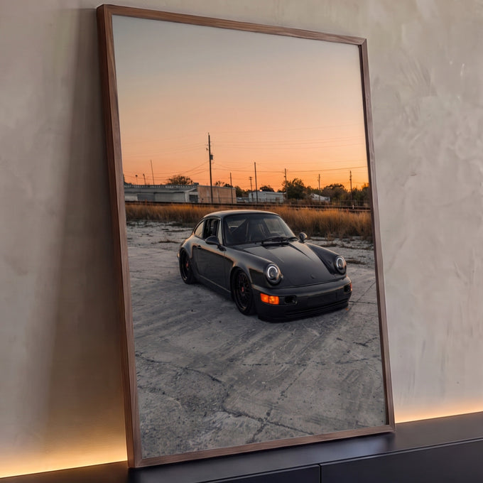 Porsche 911 preto rebaixado em pátio de concreto sob céu laranja de pôr do sol, quadro decorativo