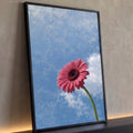 Flor gerbera rosa de caule verde erguida contra céu azul com nuvens brancas, quadro decorativo