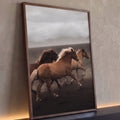 Três cavalos marrons galopando em areia vulcânica escura com montanhas na névoa, quadro decorativo
