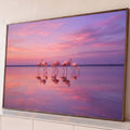 Flamingos cor-de-rosa refletidos em lago calmo sob céu rosa e lilás ao pôr do sol, quadro decorativo