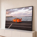 Porsche 911 laranja com aerofólio à beira-mar, skyline e céu nublado ao entardecer, quadro decorativo