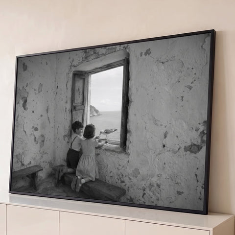Duas crianças alimentam gaivota em janela de casa rústica à beira-mar, foto preto e branco, quadro decorativo
