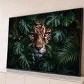 Rosto de onça-pintada com olhos âmbar espreitando entre folhas de monstera e palmeiras, quadro decorativo
