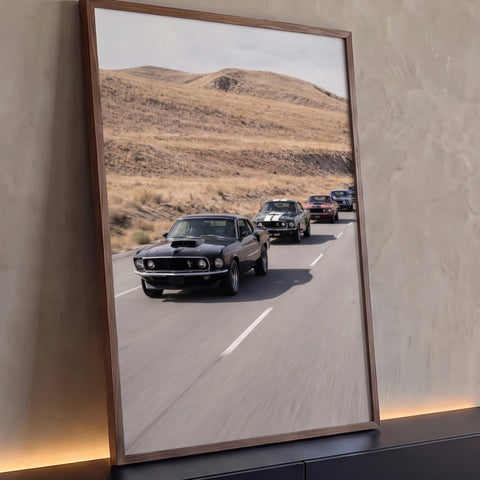 Comboio de Ford Mustangs clássicos preto, vermelho e azul em estrada entre colinas secas, quadro decorativo