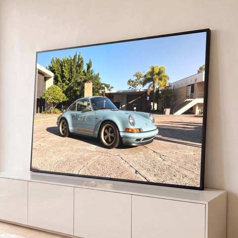 Porsche 911 clássico azul-claro com rodas retrô sob céu azul e palmeiras, quadro decorativo