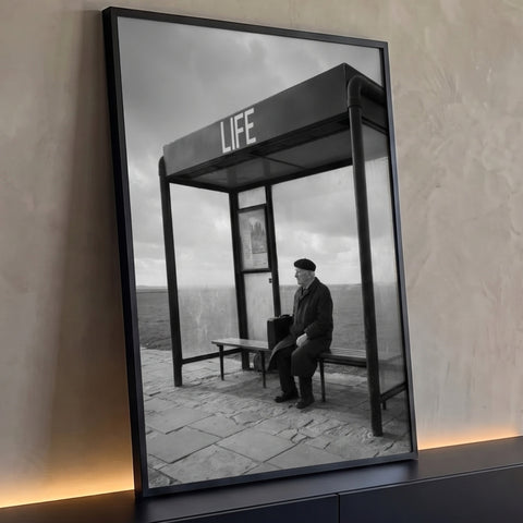 Senhor de boina com maleta sentado em ponto de ônibus escrito LIFE, em preto e branco, quadro decorativo