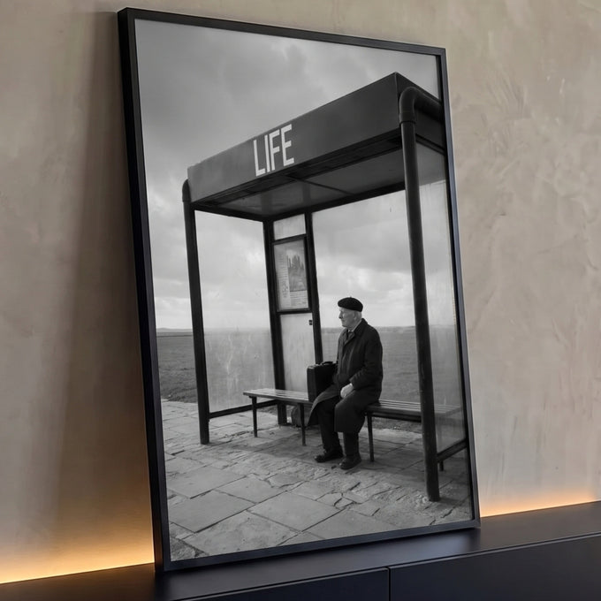 Senhor de boina com maleta sentado em ponto de ônibus escrito LIFE, em preto e branco, quadro decorativo