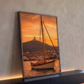 Veleiro ancorado ao pôr do sol laranja com farol na colina e vila grega branca, quadro decorativo