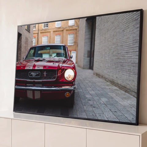Ford Mustang clássico vermelho com faixas brancas e farol aceso em rua de tijolos, quadro decorativo