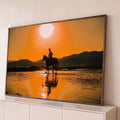 Quadro Decorativo Grande Cavaleiro ao Pôr do Sol para Sala | quadros decorativos para sala | cavaleiro em silhueta atravessando rio raso ao pôr do sol laranja com montanhas ao fundo | Porao dos Quadros