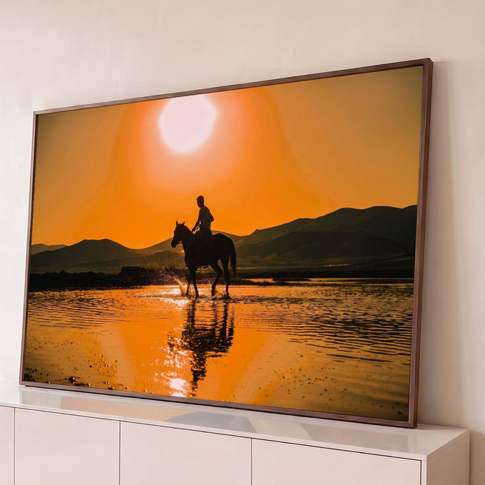 Quadro Decorativo Grande Cavaleiro ao Pôr do Sol para Sala | quadros decorativos para sala | cavaleiro em silhueta atravessando rio raso ao pôr do sol laranja com montanhas ao fundo | Porao dos Quadros