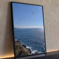 Mar azul cintilante com gaivotas voando sobre costão rochoso e vegetação, céu limpo, quadro decorativo