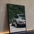 Porsche 911 clássico cinza visto de trás diante de muro de hera verde sobre paralelepípedo, quadro decorativo