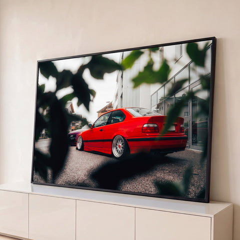 Carro esportivo vermelho rebaixado com rodas prateadas em rua entre folhas desfocadas, quadro decorativo