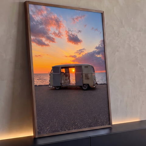 Kombi antiga de portas abertas na orla com pôr do sol laranja sobre o mar, quadro decorativo