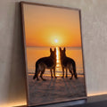 Dois pastores alemães em silhueta olhando o pôr do sol laranja sobre o mar na praia, quadro decorativo