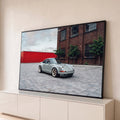 Porsche 911 clássico cinza com rodas douradas em pátio de pedras e prédio de tijolos, quadro decorativo
