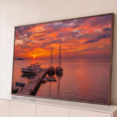 Iates e veleiros atracados em cais de madeira sob pôr do sol laranja refletido no mar, quadro decorativo