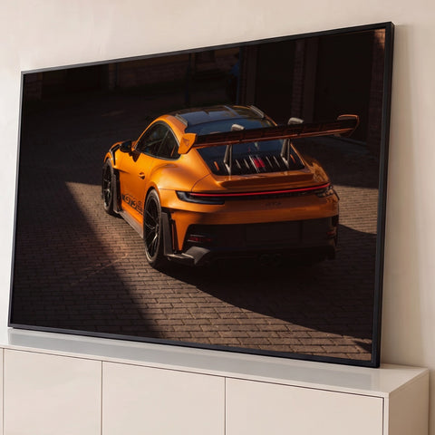 Porsche GT3 RS laranja visto de trás com aerofólio, entre luz e sombra em rua de pedra, quadro decorativo
