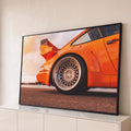 Traseira de carro esportivo laranja com roda cromada raiada e aerofólio ao pôr do sol, quadro decorativo