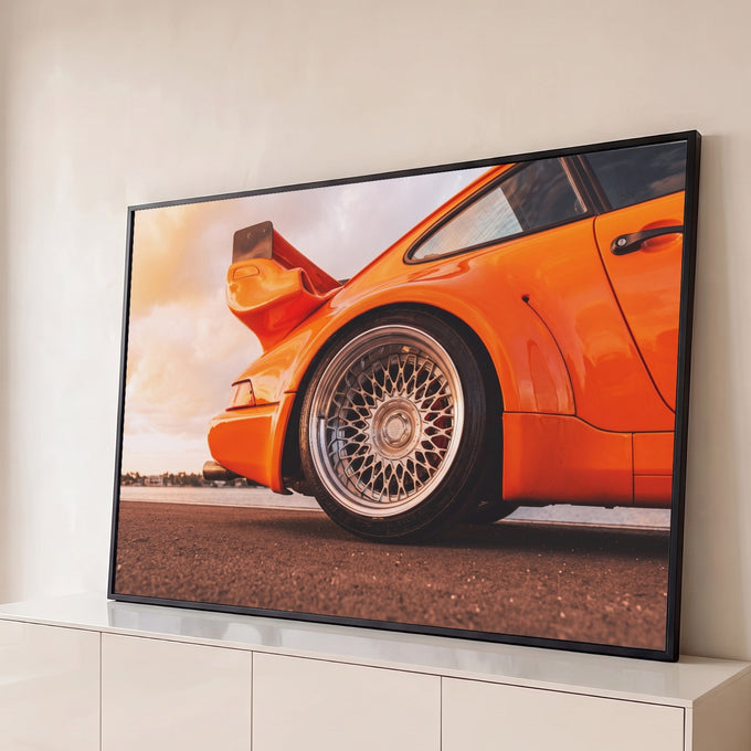 Traseira de carro esportivo laranja com roda cromada raiada e aerofólio ao pôr do sol, quadro decorativo