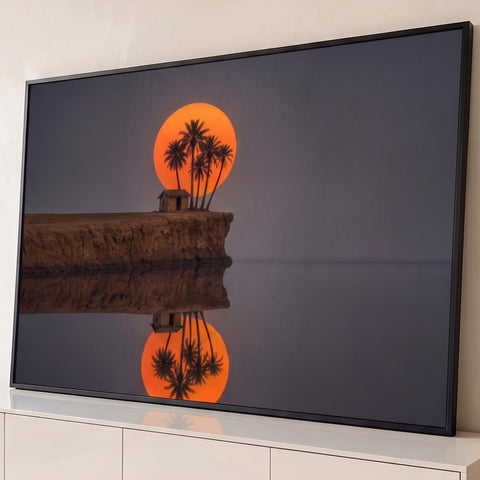 Sol laranja atrás de palmeiras e cabana, refletidos em água calma sob céu cinza, quadro decorativo