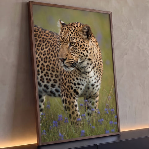 Leopardo em close olhando de lado, entre flores roxas em campo verde, quadro decorativo