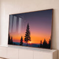 Pinheiro em silhueta ao pôr do sol com lua crescente, montanhas e céu laranja e roxo, quadro decorativo