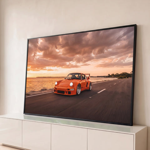 Porsche clássico laranja com aerofólio em estrada à beira-mar sob céu de pôr do sol, quadro decorativo