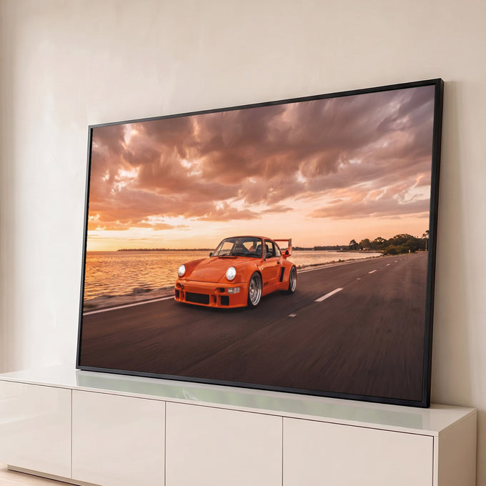 Porsche clássico laranja com aerofólio em estrada à beira-mar sob céu de pôr do sol, quadro decorativo