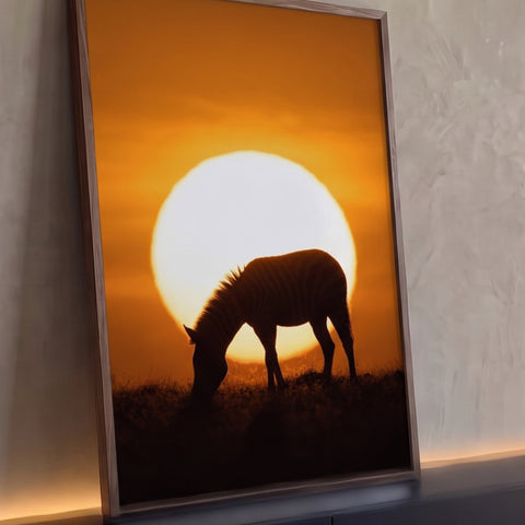 Silhueta de zebra pastando diante de sol gigante em céu laranja na savana africana, quadro decorativo