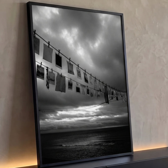Varal com fotografias e pregadores sobre o mar sob céu nublado em preto e branco, quadro decorativo