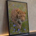 Leopardo agachado à espreita, olhar intenso, em campo verde com flores lilás, quadro decorativo