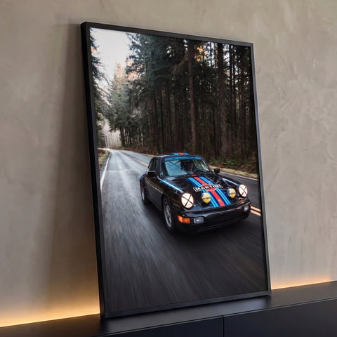 Porsche 911 preto com faixas Martini em velocidade numa estrada cercada por pinheiros, quadro decorativo