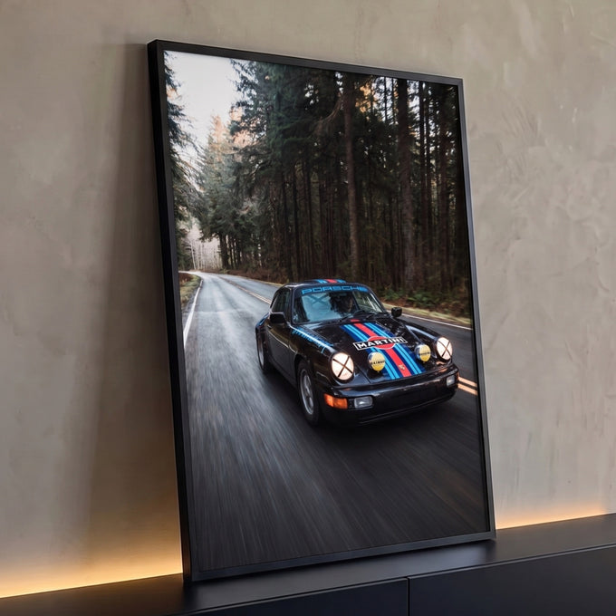 Porsche 911 preto com faixas Martini em velocidade numa estrada cercada por pinheiros, quadro decorativo