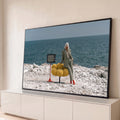 Mulher de terno xadrez e botas vermelhas com TV retrô e poltrona amarela à beira-mar, quadro decorativo