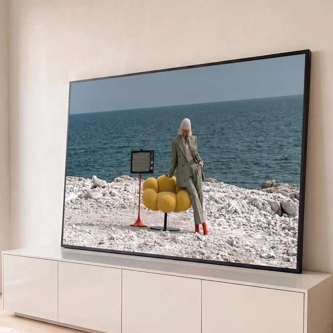 Mulher de terno xadrez e botas vermelhas com TV retrô e poltrona amarela à beira-mar, quadro decorativo