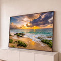 Praia ao pôr do sol com mar turquesa, ondas suaves e rochas cobertas de musgo verde, quadro decorativo