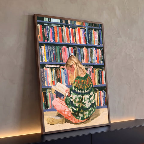 Mulher loira de suéter verde lendo sentada no chão diante de estante de livros coloridos, quadro decorativo