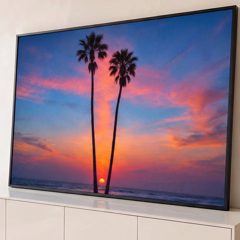 Duas palmeiras altas em silhueta diante do pôr do sol sobre o mar, céu azul e laranja, quadro decorativo