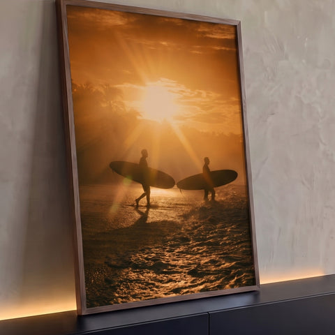 Dois surfistas em silhueta com pranchas caminhando no mar ao pôr do sol laranja, quadro decorativo